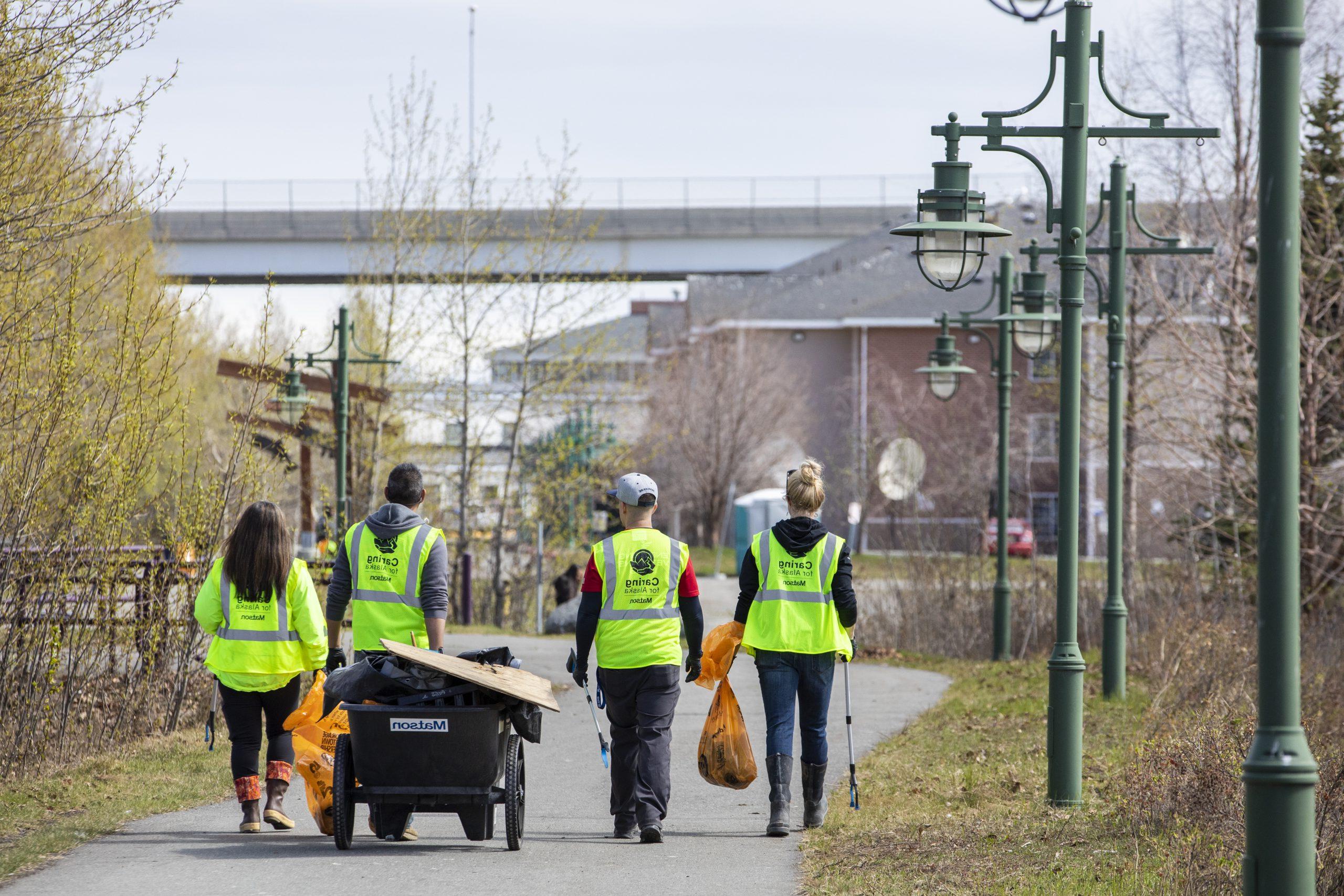 志愿者们穿着黄色的安全背心，推着一辆手推车，提着装满垃圾的橙色袋子，沿着船溪走着.